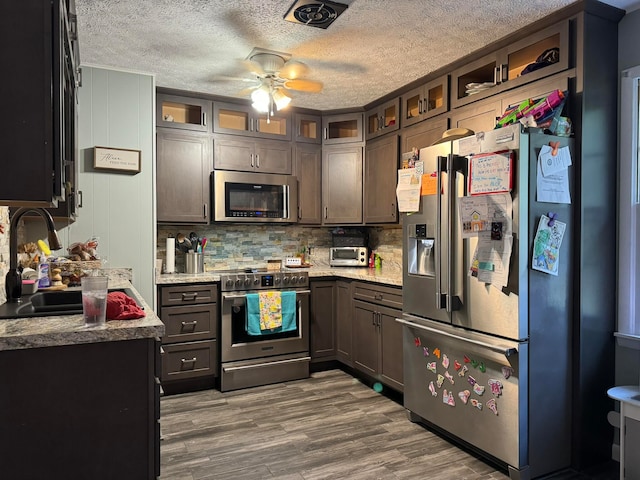 kitchen with ceiling fan, appliances with stainless steel finishes, light stone counters, and dark hardwood / wood-style flooring