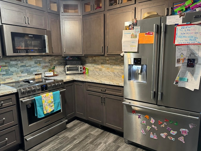 kitchen with light stone countertops, stainless steel appliances, backsplash, and dark brown cabinetry