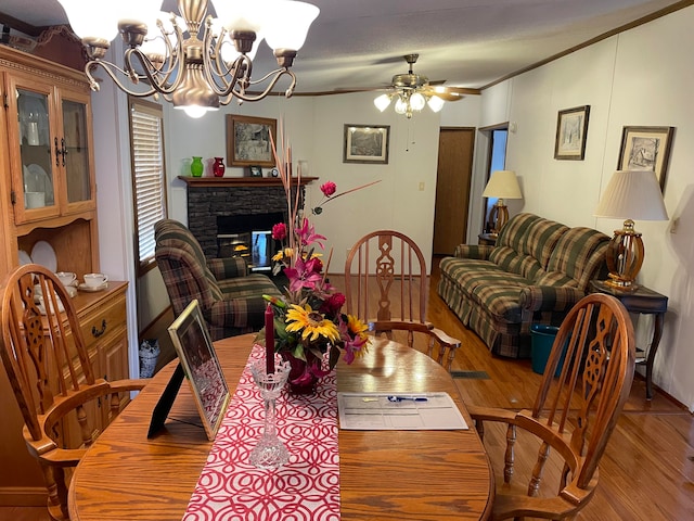 dining room featuring crown molding, a fireplace, light hardwood / wood-style floors, and ceiling fan with notable chandelier