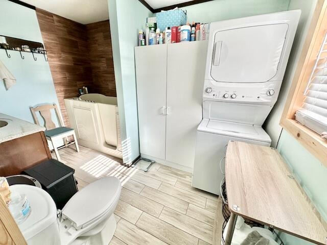 laundry room with stacked washer and clothes dryer, light hardwood / wood-style floors, and wooden walls