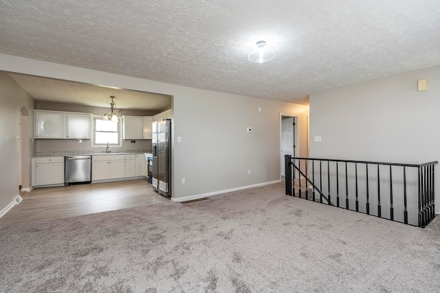 unfurnished living room with light carpet, a textured ceiling, a chandelier, and sink