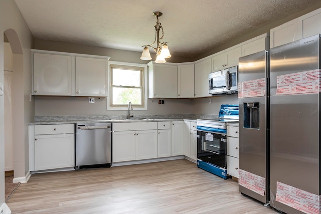 kitchen featuring white cabinets, stainless steel appliances, light wood-type flooring, and decorative light fixtures