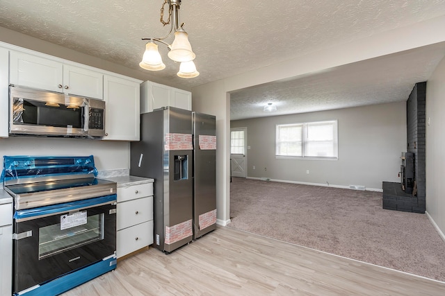 kitchen featuring light hardwood / wood-style floors, white cabinets, pendant lighting, stainless steel appliances, and a textured ceiling