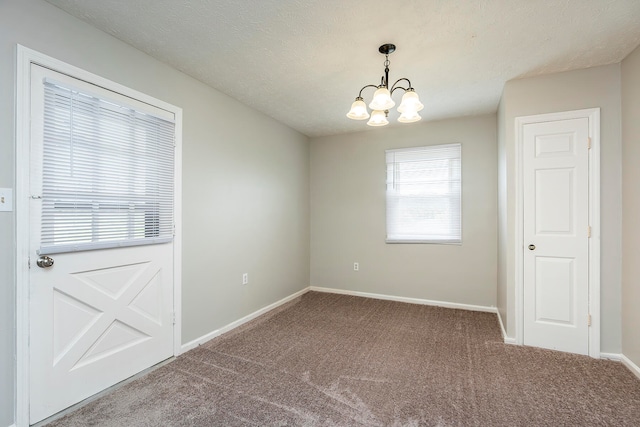 empty room featuring a notable chandelier, a textured ceiling, and carpet