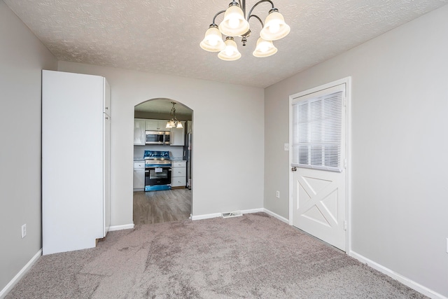 carpeted spare room featuring a textured ceiling and a notable chandelier