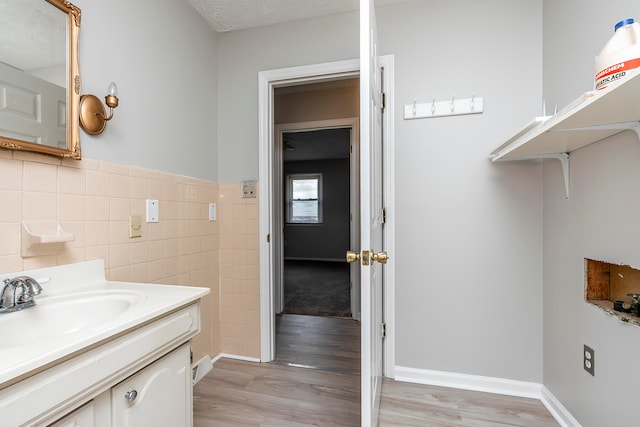 bathroom with wood-type flooring, vanity, tile walls, and a textured ceiling