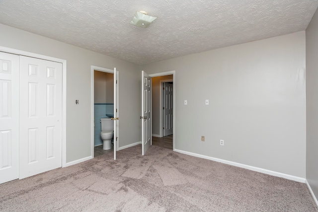 unfurnished bedroom featuring a textured ceiling, ensuite bath, light colored carpet, and a closet