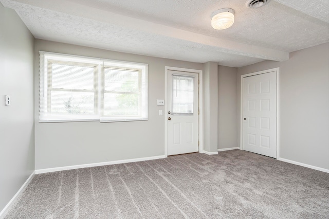 unfurnished room with a textured ceiling, beam ceiling, and carpet flooring