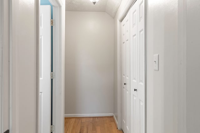 hallway featuring a textured ceiling, light hardwood / wood-style floors, and vaulted ceiling