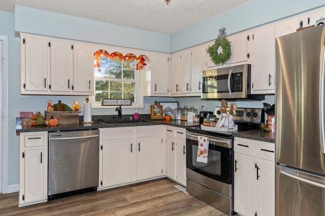 kitchen with sink, a textured ceiling, white cabinetry, hardwood / wood-style flooring, and appliances with stainless steel finishes