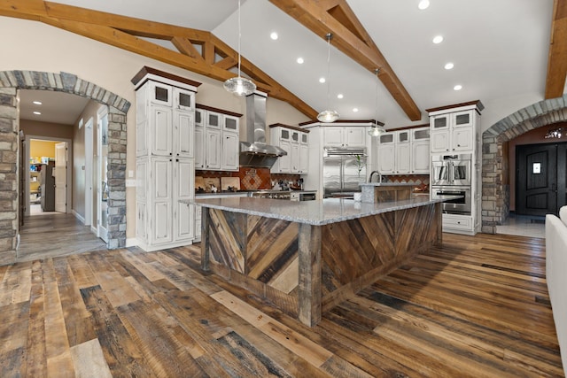 kitchen featuring hanging light fixtures, light stone counters, tasteful backsplash, wall chimney exhaust hood, and a spacious island