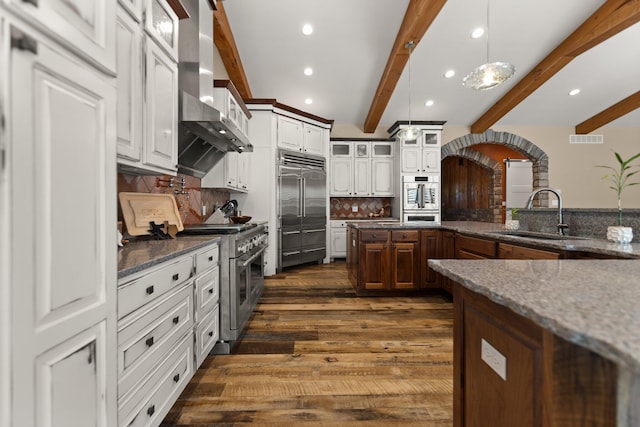 kitchen featuring dark wood-type flooring, premium appliances, pendant lighting, beamed ceiling, and wall chimney range hood