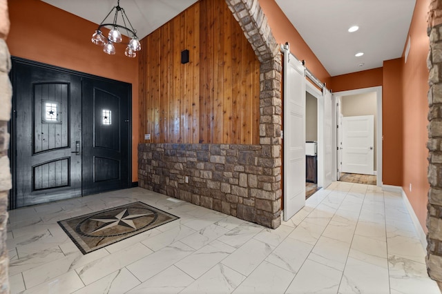 entrance foyer with wood walls, a barn door, and a chandelier