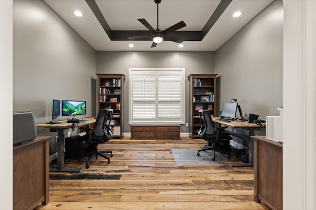 office area featuring ceiling fan, light wood-type flooring, and a tray ceiling