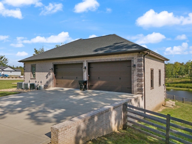 view of property exterior featuring a garage, central AC, a yard, an outdoor structure, and a water view