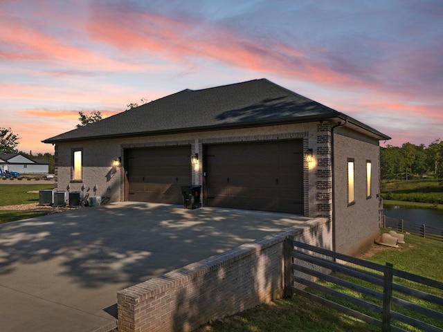 property exterior at dusk with central AC unit, a garage, a lawn, and an outbuilding