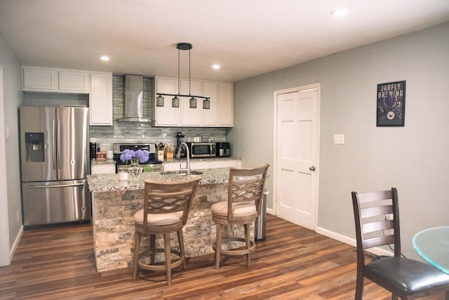 kitchen with white cabinetry, dark wood-type flooring, wall chimney exhaust hood, stainless steel appliances, and a kitchen island with sink