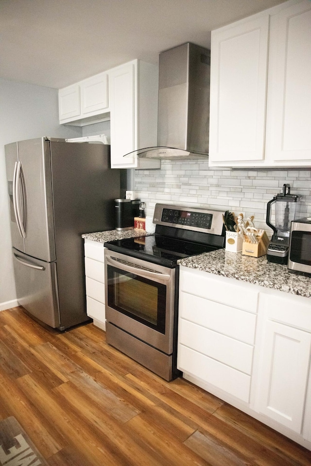 kitchen featuring appliances with stainless steel finishes, tasteful backsplash, white cabinets, hardwood / wood-style flooring, and wall chimney range hood