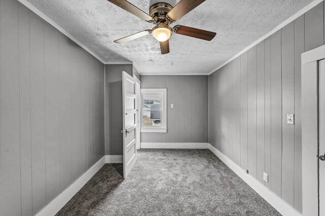 carpeted empty room featuring a textured ceiling, ornamental molding, wooden walls, and ceiling fan