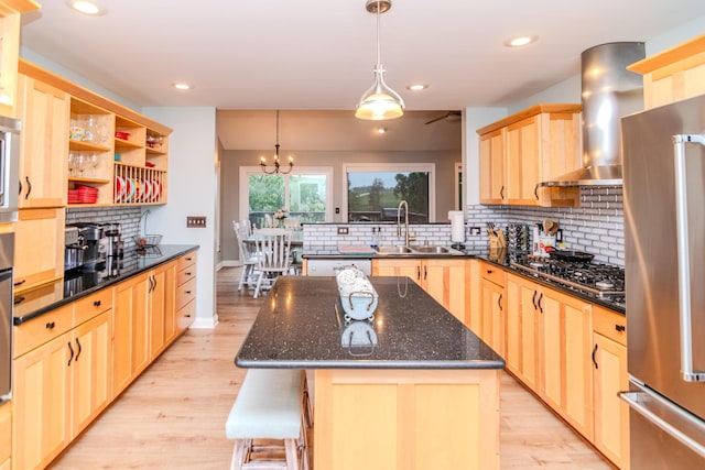 kitchen with light brown cabinetry, sink, a center island, stainless steel appliances, and wall chimney range hood