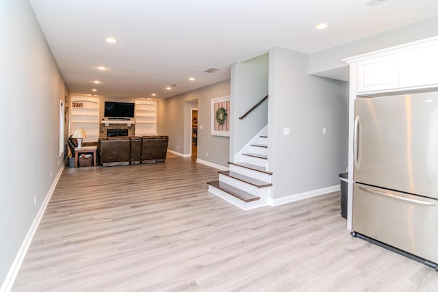 kitchen featuring white cabinetry, light wood-type flooring, stainless steel refrigerator, built in features, and a fireplace