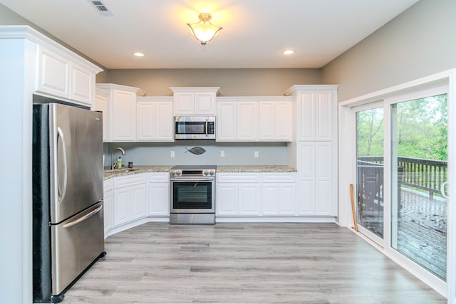 kitchen with light stone counters, stainless steel appliances, light hardwood / wood-style flooring, and white cabinets