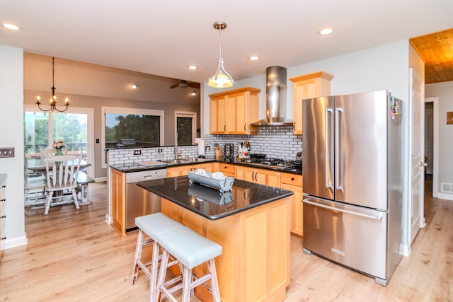 kitchen with wall chimney exhaust hood, a center island, appliances with stainless steel finishes, and light hardwood / wood-style flooring