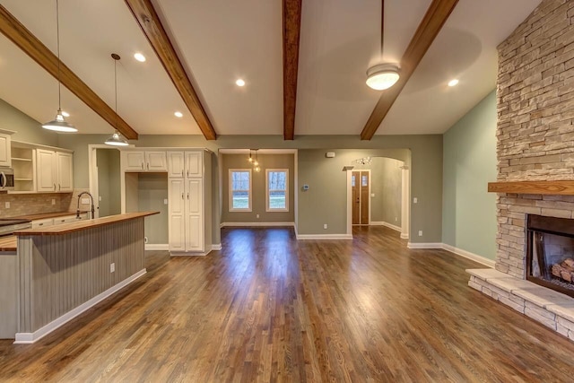 unfurnished living room with vaulted ceiling with beams, a stone fireplace, sink, and dark wood-type flooring