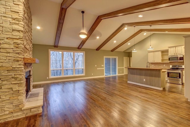 unfurnished living room with lofted ceiling with beams, dark wood-type flooring, sink, a stone fireplace, and ceiling fan