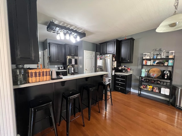 kitchen featuring appliances with stainless steel finishes, a breakfast bar, kitchen peninsula, light wood-type flooring, and sink