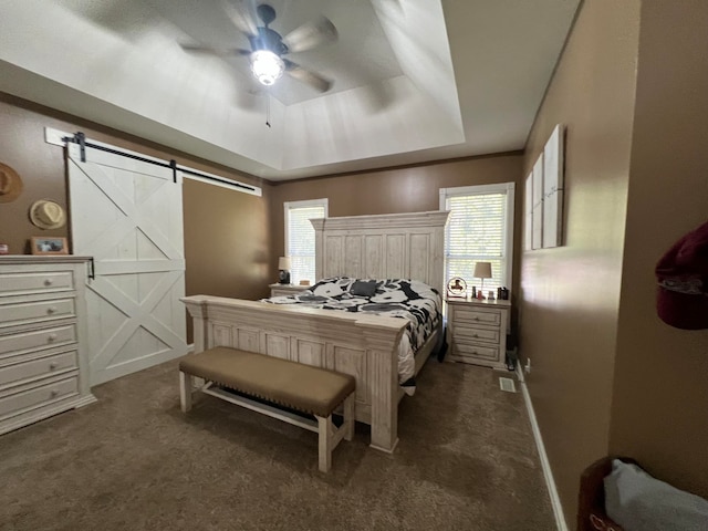 carpeted bedroom with a tray ceiling, ceiling fan, and a barn door