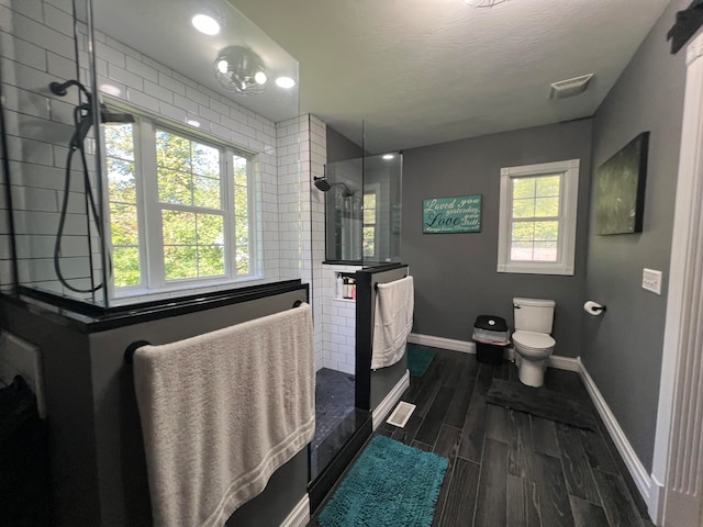 bathroom with toilet, plenty of natural light, and a tile shower