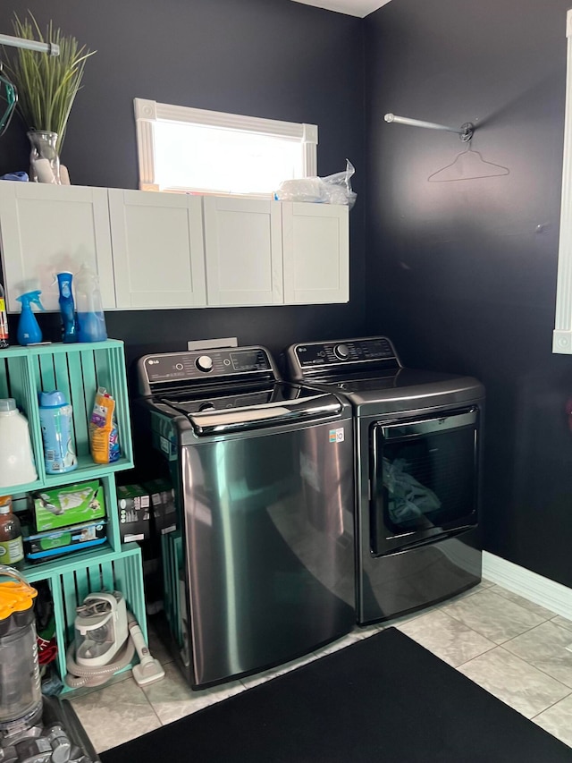 clothes washing area featuring washing machine and dryer, light tile patterned floors, and cabinets