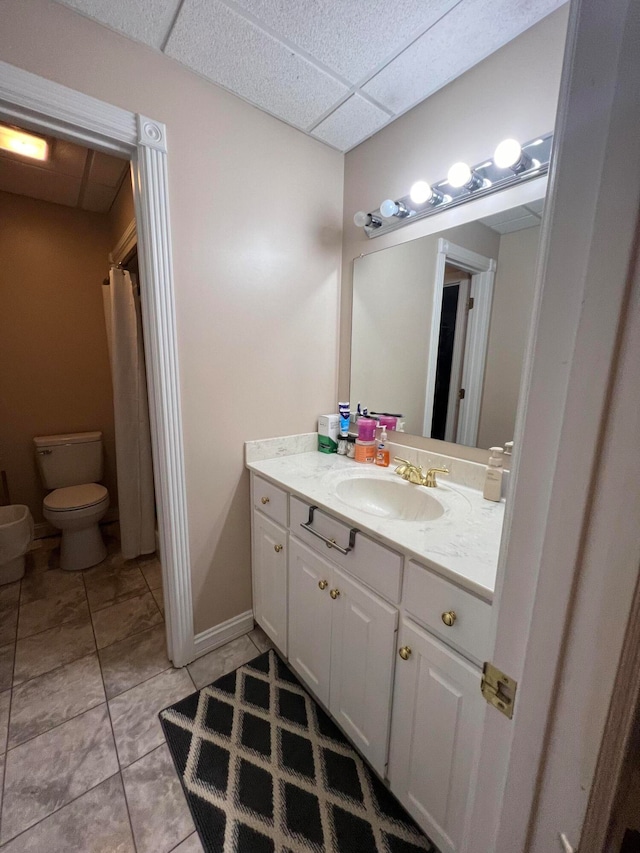 bathroom with a drop ceiling, vanity, toilet, and tile patterned floors