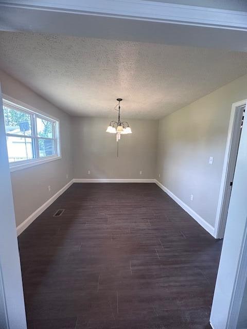 unfurnished room featuring a chandelier, a textured ceiling, and dark hardwood / wood-style flooring