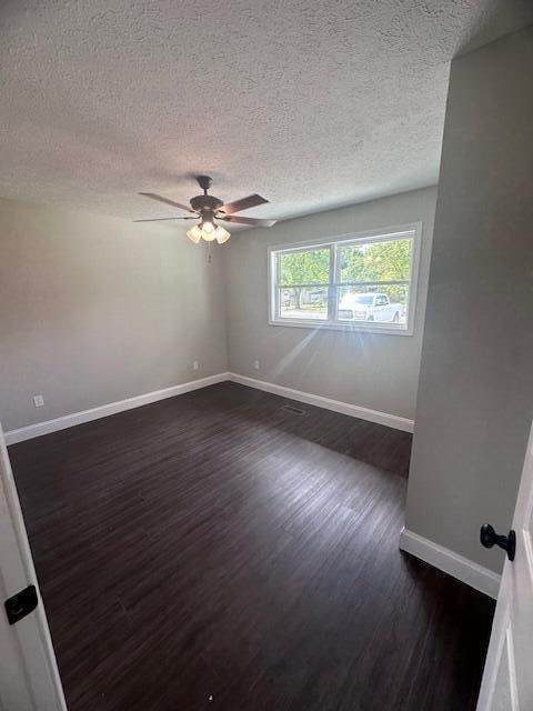 unfurnished room featuring ceiling fan, dark wood-type flooring, and a textured ceiling