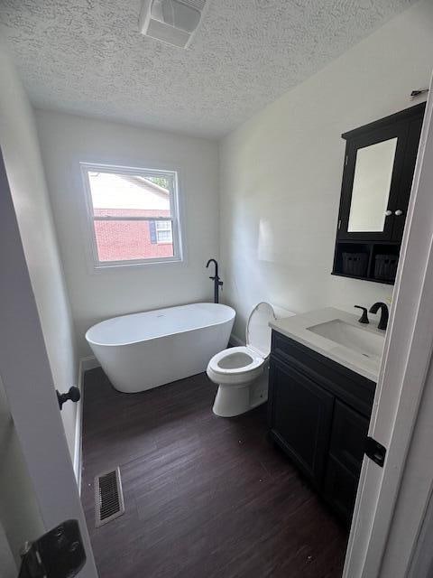 bathroom featuring a textured ceiling, a bath, hardwood / wood-style flooring, vanity, and toilet