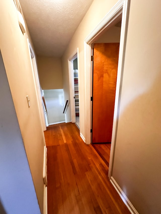 corridor with a textured ceiling and dark wood-type flooring