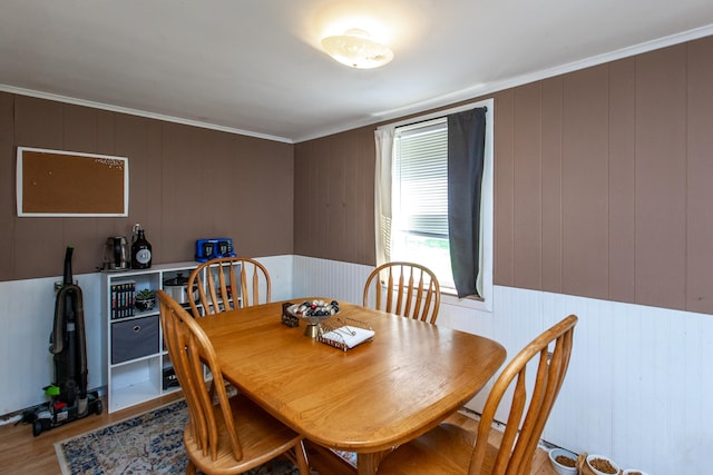 dining space featuring crown molding, wooden walls, and light hardwood / wood-style flooring