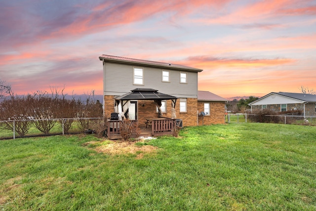 back house at dusk with a gazebo, a deck, and a lawn