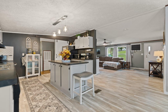 kitchen with white cabinetry, ceiling fan with notable chandelier, a textured ceiling, light hardwood / wood-style flooring, and ornamental molding