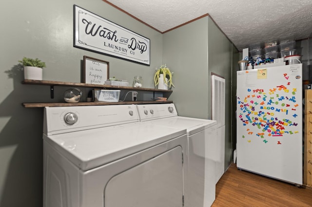 clothes washing area featuring a textured ceiling, washing machine and dryer, ornamental molding, and hardwood / wood-style flooring