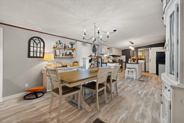 dining room featuring a textured ceiling, light hardwood / wood-style flooring, a notable chandelier, crown molding, and a barn door