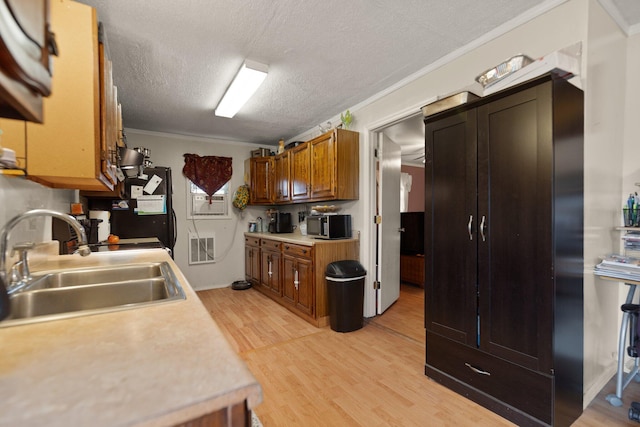 kitchen featuring a textured ceiling, crown molding, sink, and light hardwood / wood-style flooring