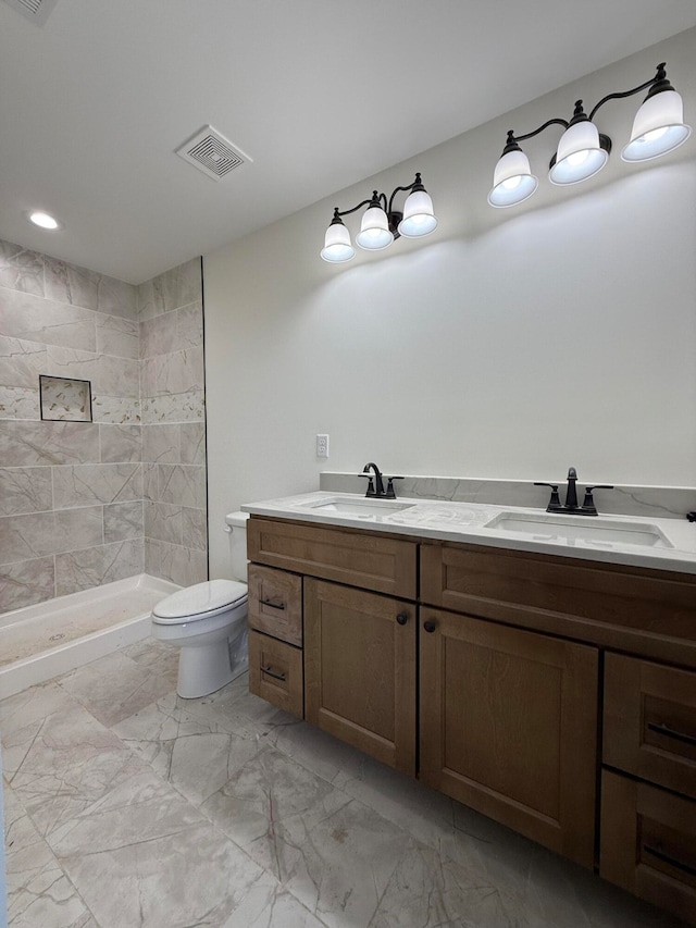 bathroom with visible vents, tiled shower, toilet, and a sink