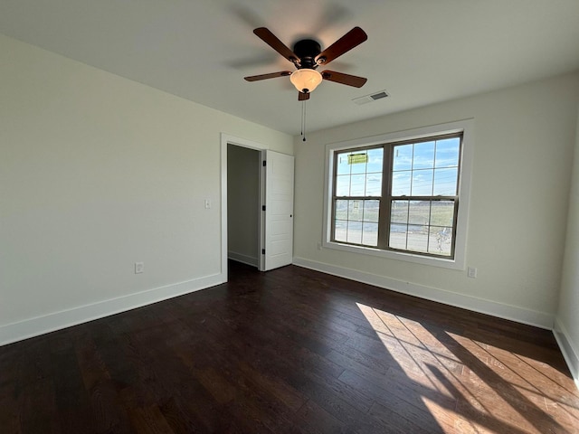 spare room with visible vents, ceiling fan, dark wood-type flooring, and baseboards