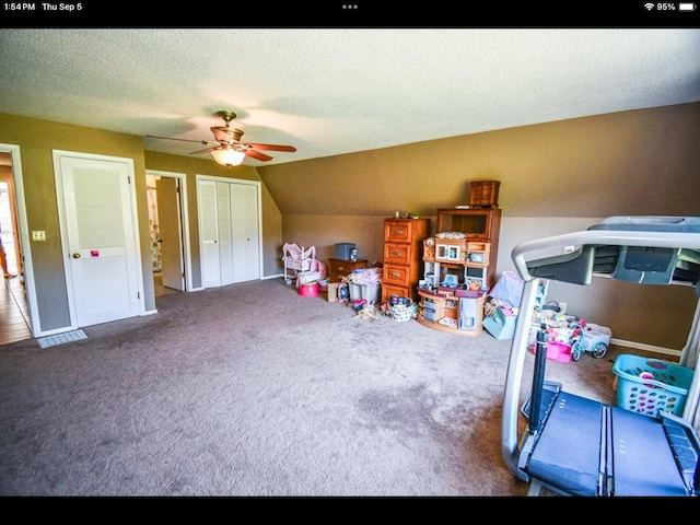 recreation room with a textured ceiling, vaulted ceiling, ceiling fan, and dark carpet