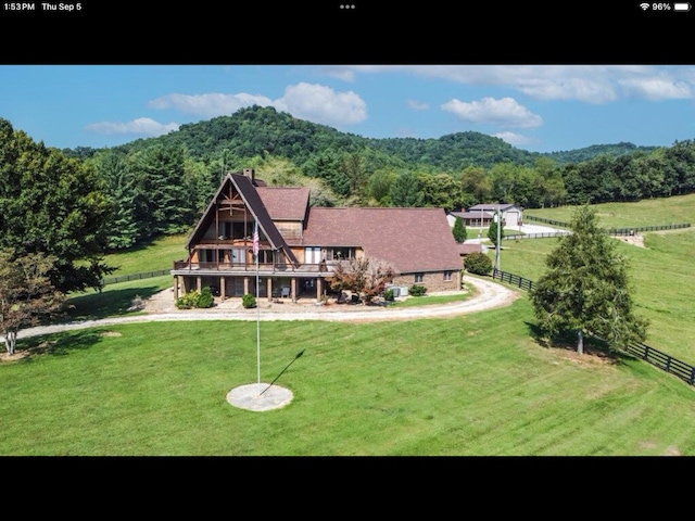 rear view of property featuring a lawn, a mountain view, and a rural view