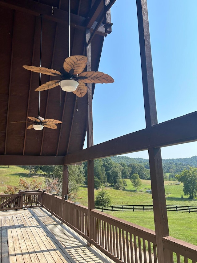 wooden terrace featuring ceiling fan, a rural view, and a lawn