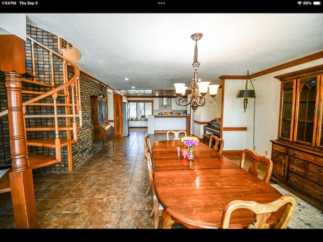 dining room with a notable chandelier, a textured ceiling, brick wall, and crown molding